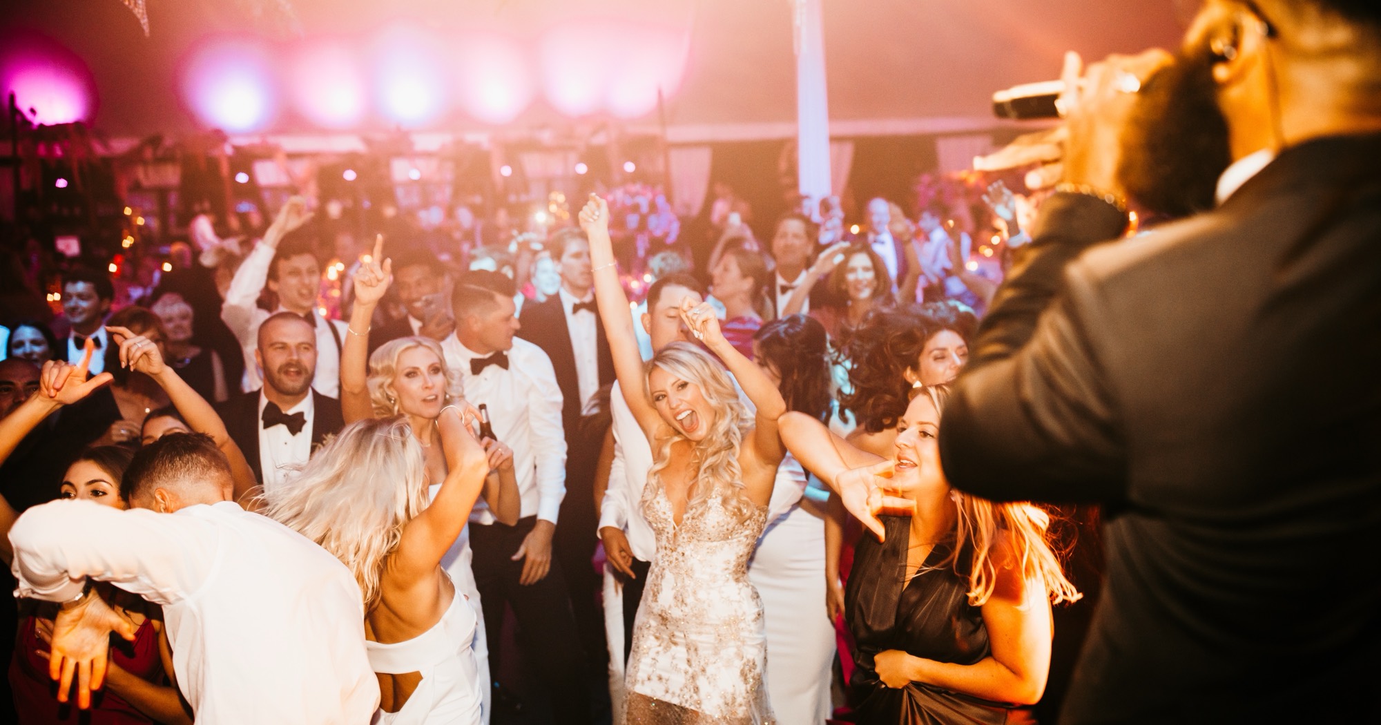A packed dance floor of guests in black tie, arms up, the band playing behind them.